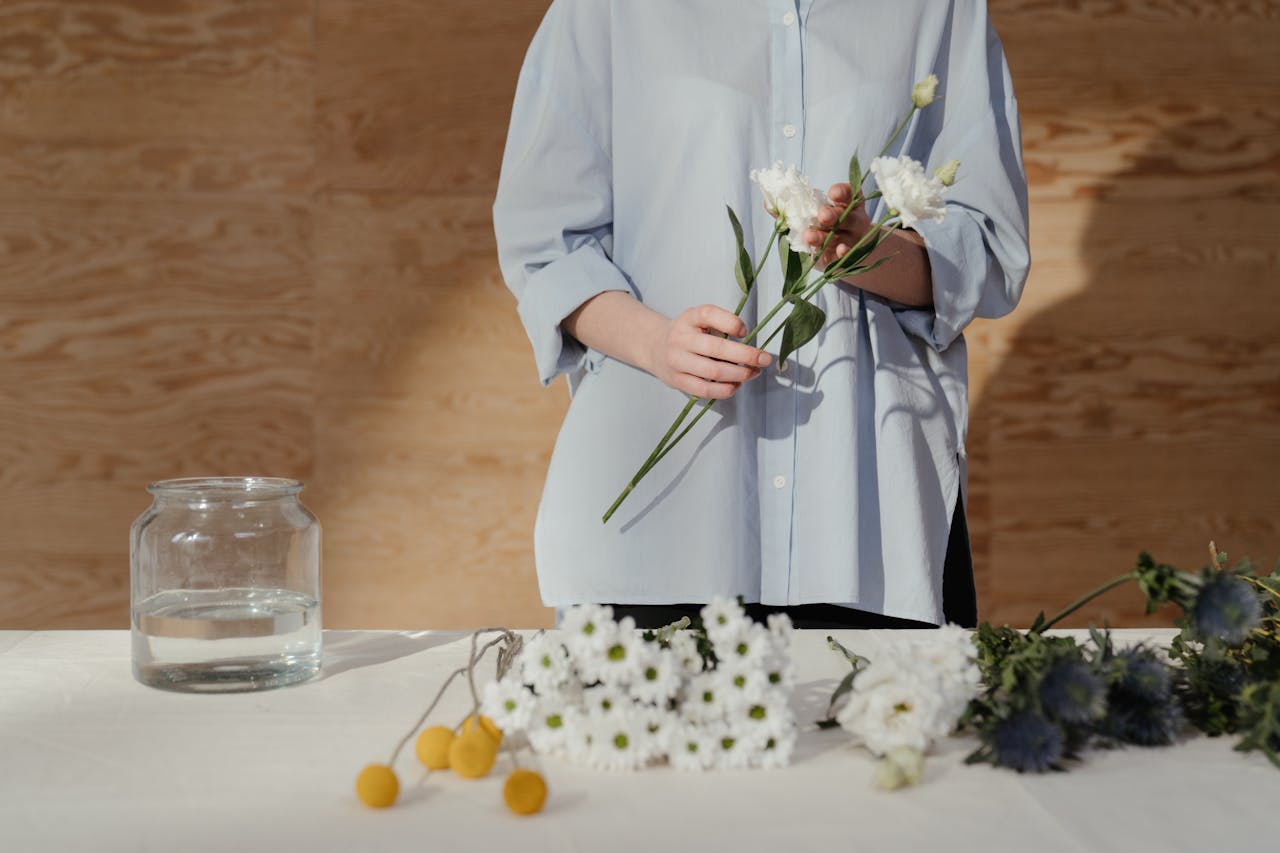 A florist arranges a bouquet of white flowers in a bright, minimalist setting.